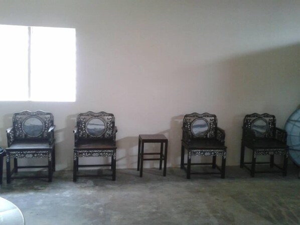 Una habitación con cuatro sillas decorativas y una mesita pequeña, dispuestas frente a una pared lisa con un ventanal.