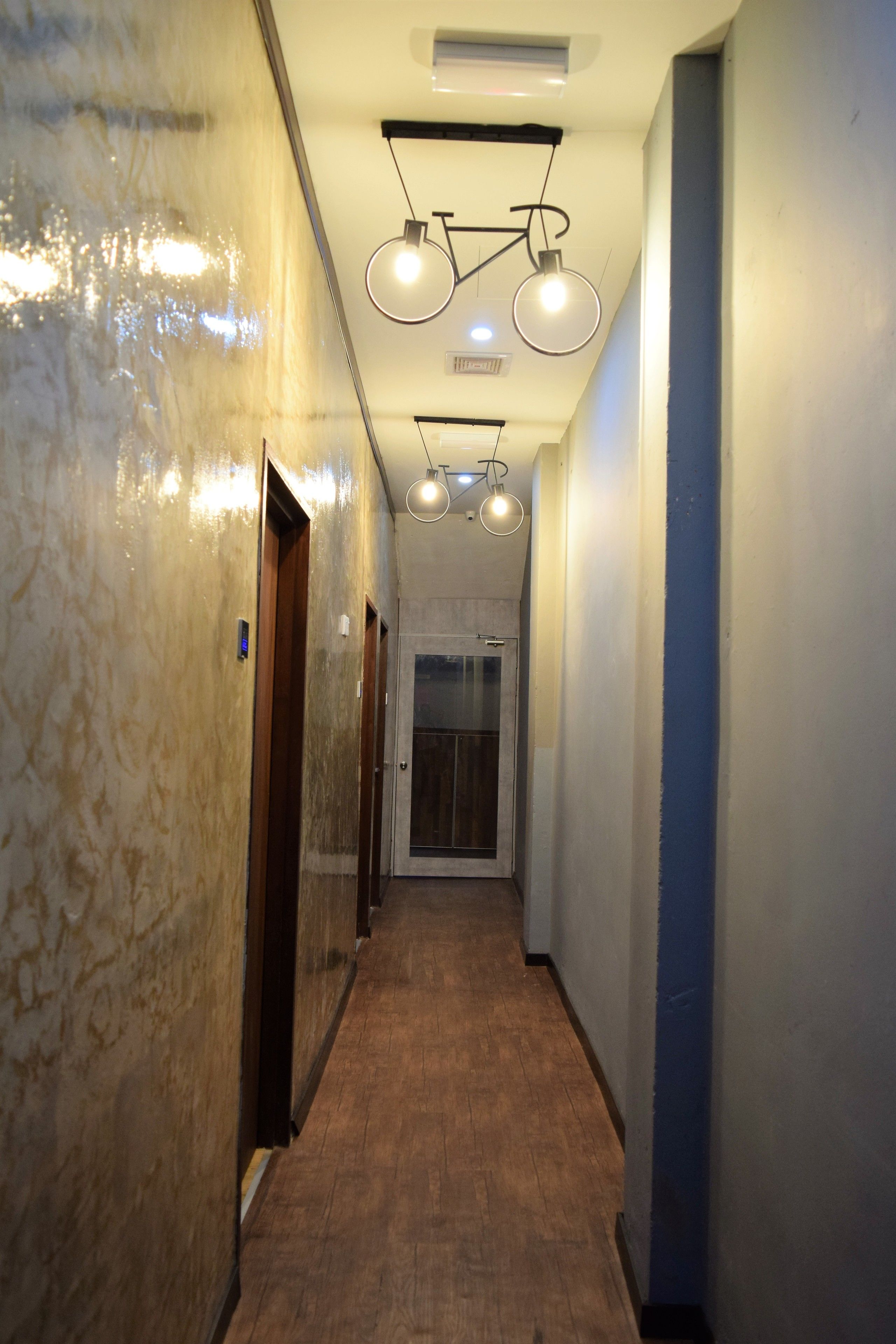 A hallway with marble walls, wooden floors, and pendant lighting.