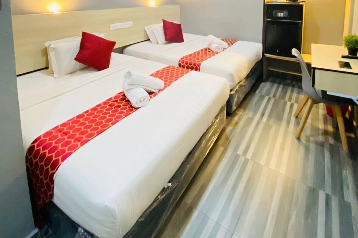 A hotel room with two beds, a desk, a chair, and a microwave.