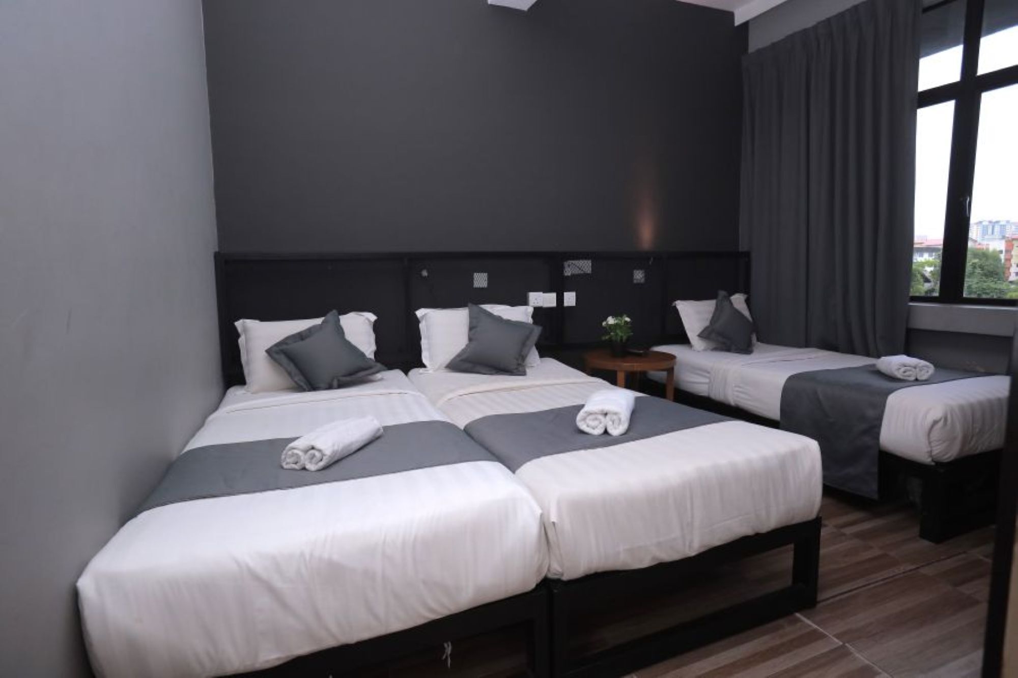 Quarto de hotel com uma cama grande, duas camas menores, uma mesa de cabeceira e uma janela com cortinas.