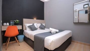 A hotel room with a bed, a desk with a chair, a mirror, and a small trash bin.