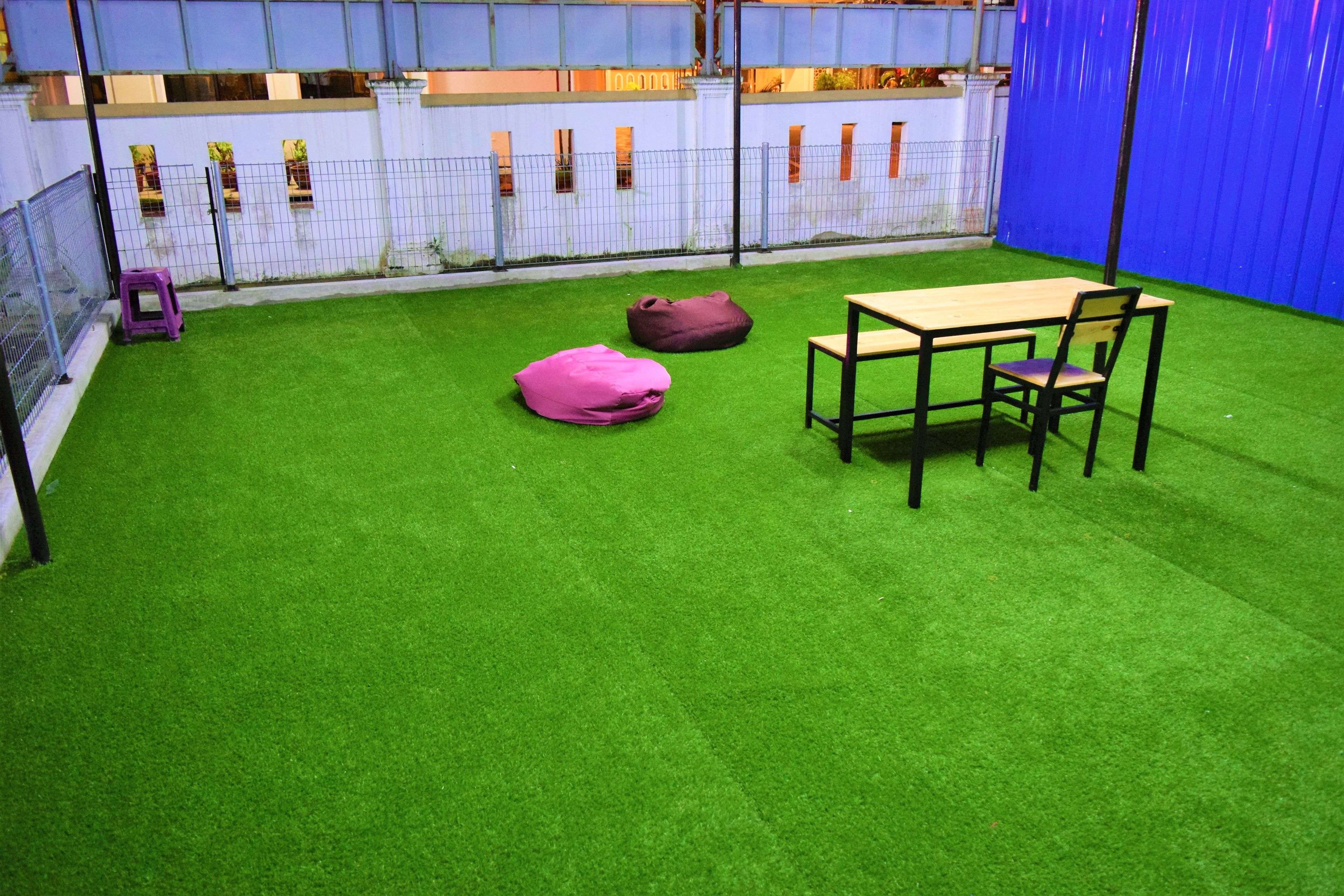A small outdoor area with artificial grass, a wooden table with chairs, and two bean bags.