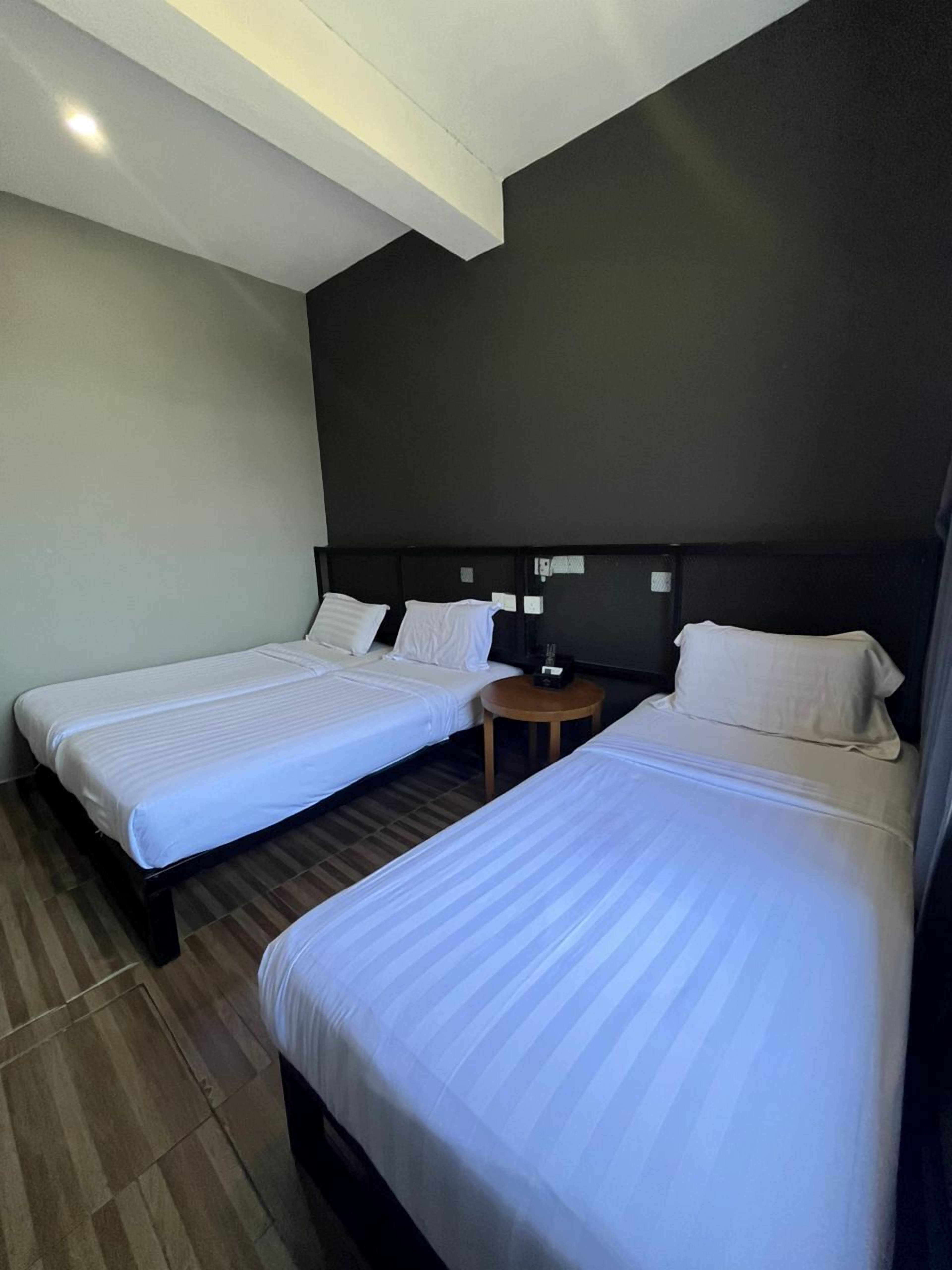 A hotel room with two single beds, a small round table, and a dark-colored headboard.