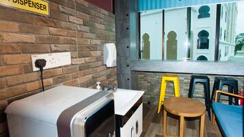 Una zona de cocina con pared de ladrillo, un lavabo, una cafetera, dispensador de jabón para manos y una ventana con vista a un edificio.