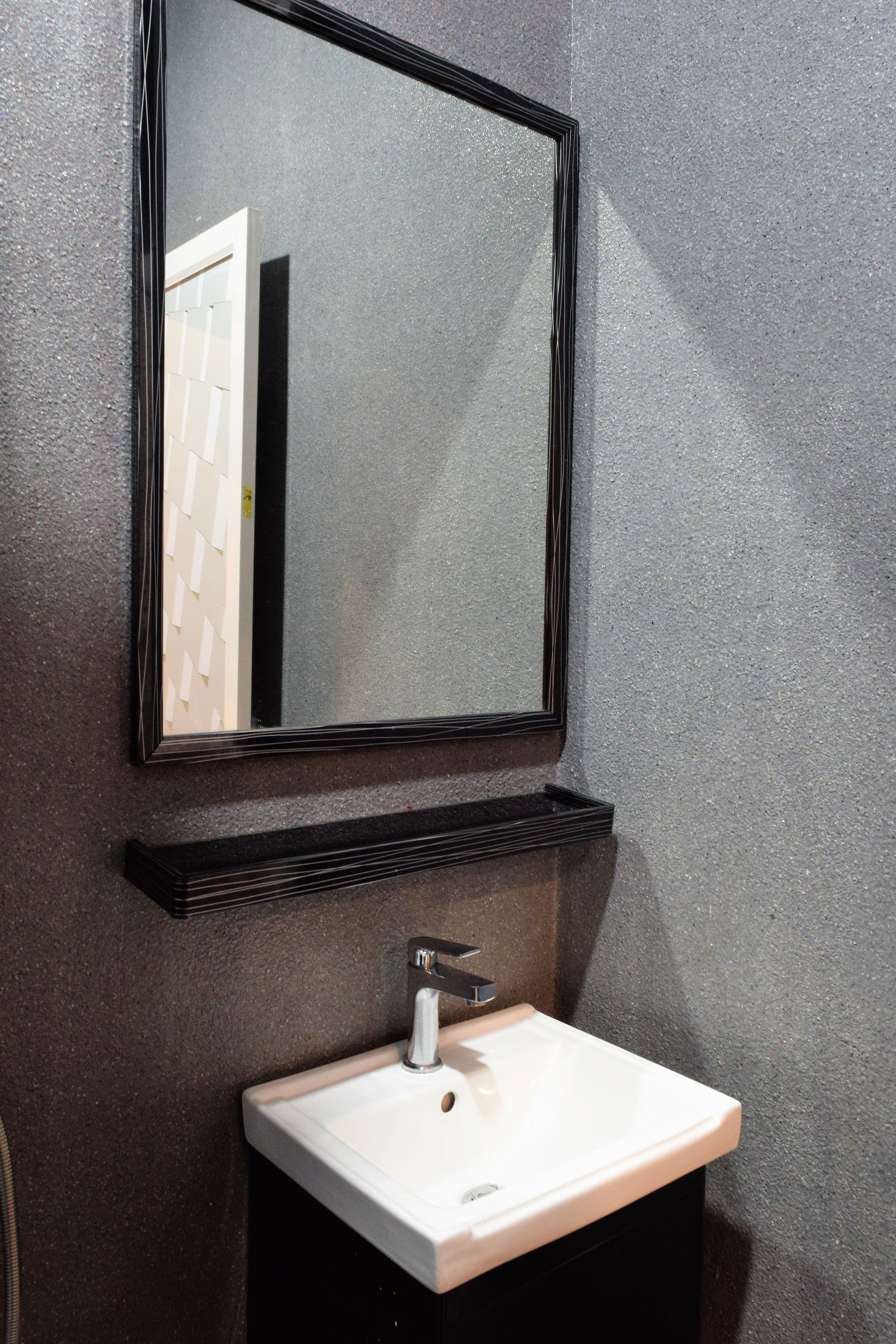 Une salle de bain avec un lavabo blanc, un miroir à cadre noir et une étagère noire située sous le miroir.