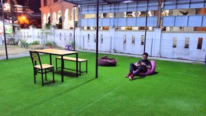 Un espacio exterior con césped, una mesa y sillas, un sillón de pie rosa y una persona sentada en un sillón de pie.