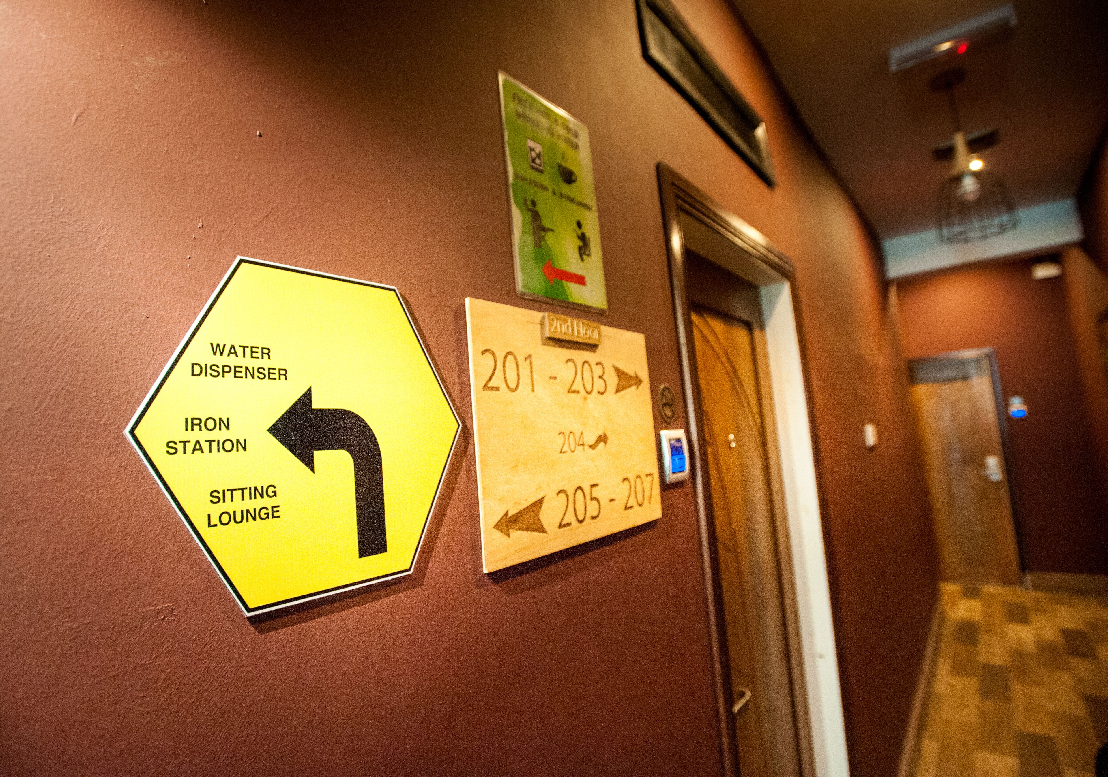 A hallway with directional signs for amenities like a water dispenser, iron station, and sitting lounge.