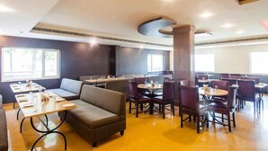 A restaurant with high tables and booths, a large pillar, and a bright interior. - Hotel Shubham Majesty (Mathura)