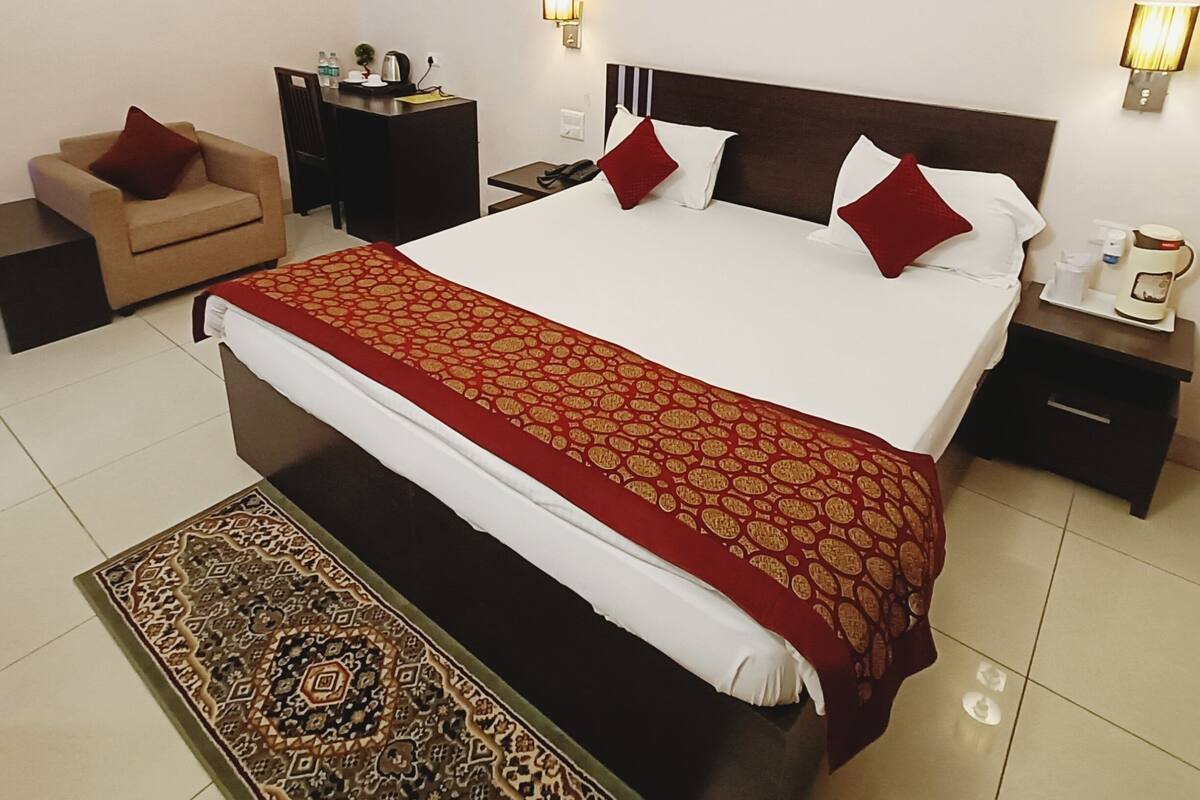 A hotel room with a large bed, two bedside tables, a desk, a chair, and a patterned rug.