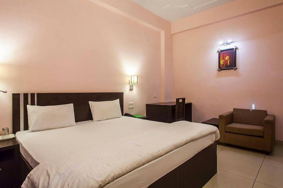 A hotel room with a large bed, a small table, a chair, and a wall-mounted light fixture.