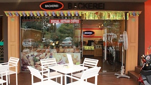 A storefront with a sign reading "SPECIAL VIETNAM COFFEE" and a "BACKEREI" sign above. Inside, there are white chairs and tables arranged for seating. - Your Hotel (Genting Highlands)