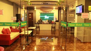 A hotel reception area with a reception desk, a waiting area with a red sofa, and a TV screen displaying a welcome message. - Your Hotel (Genting Highlands)