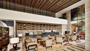 A spacious lobby with a high ceiling, a seating area with armchairs and sofas, a reception desk, and a display case with items. - Radisson Blu Faridabad (Faridabad)
