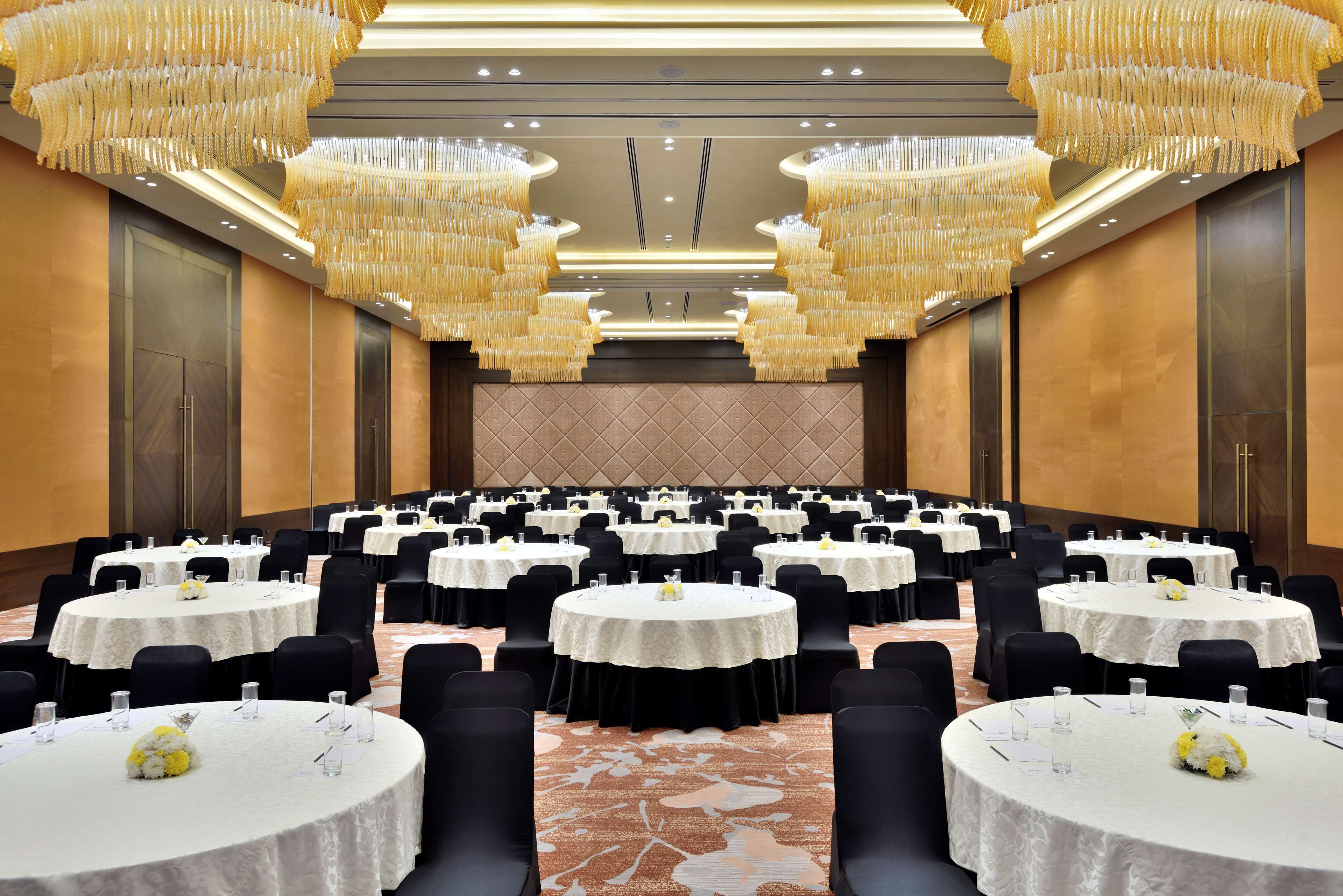 A large conference room with multiple round tables, black chairs, and chandeliers.