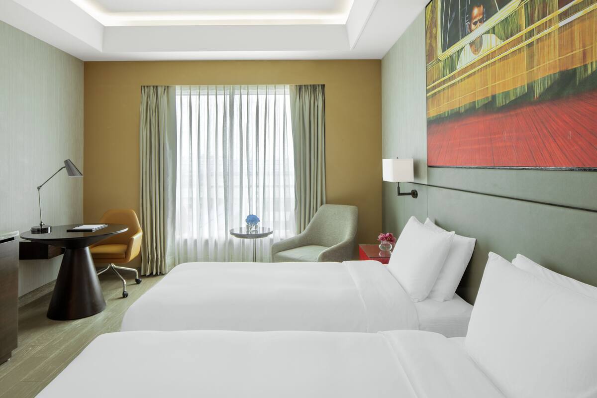Habitación de hotel con una cama grande, un escritorio, una silla, una mesita con un florero y un cuadro en la pared.