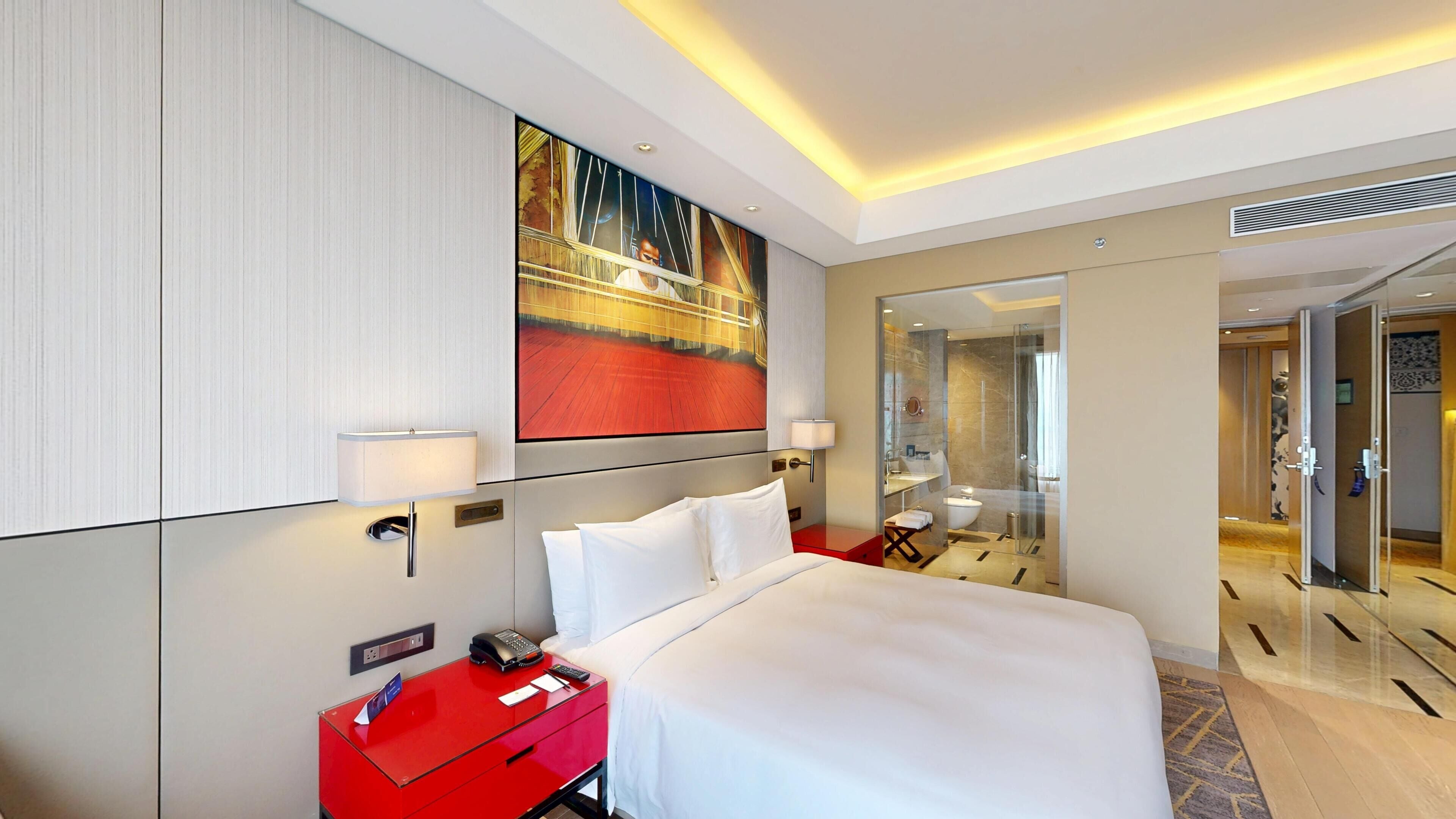 Een hotelkamer met een bed, een rode nachtkastje, een telefoon en een schilderij aan de muur.