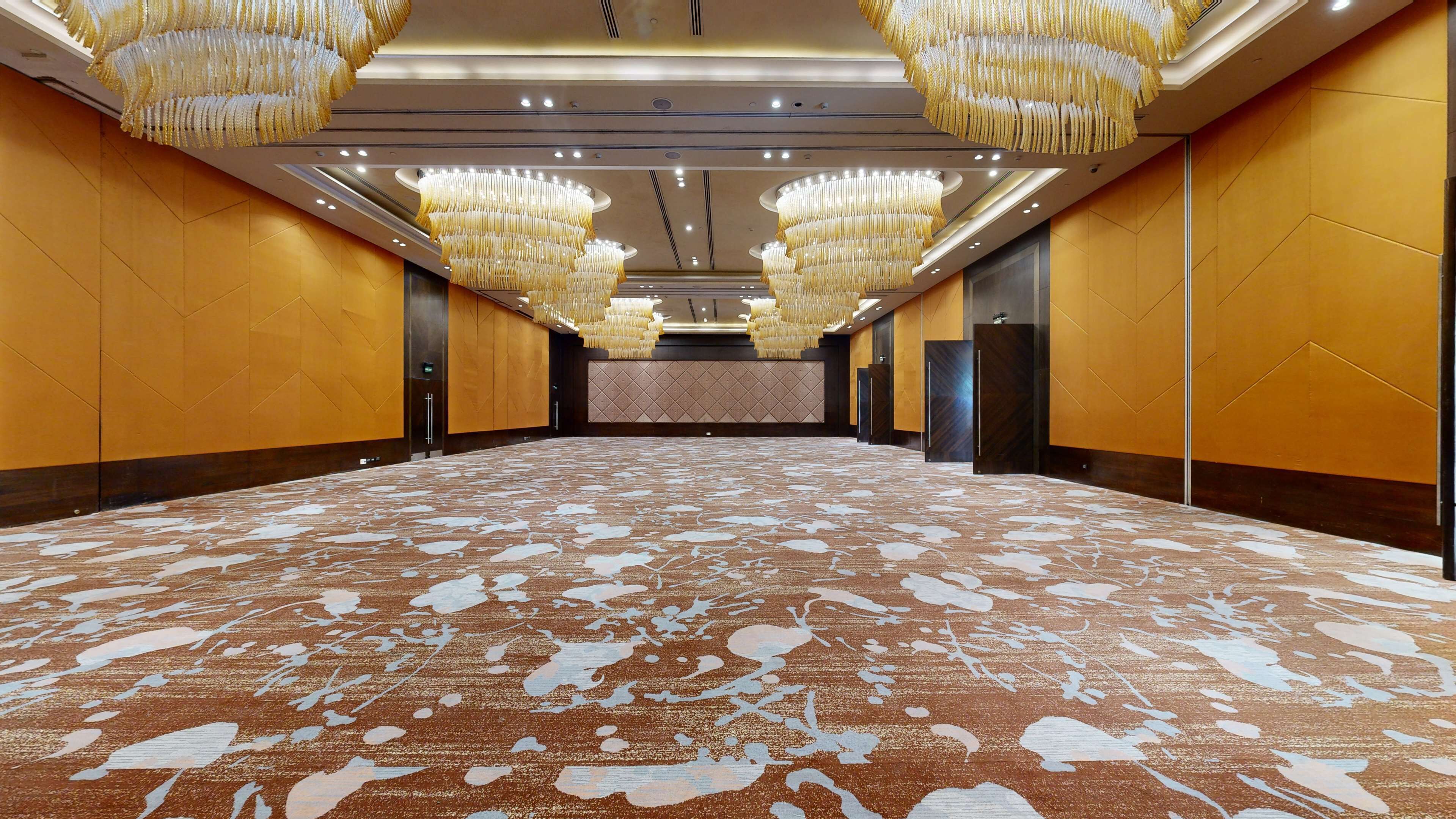 Une salle de conférence spacieuse, dotée d’un tapis à motifs, de grands lustres et d’un design moderne.
