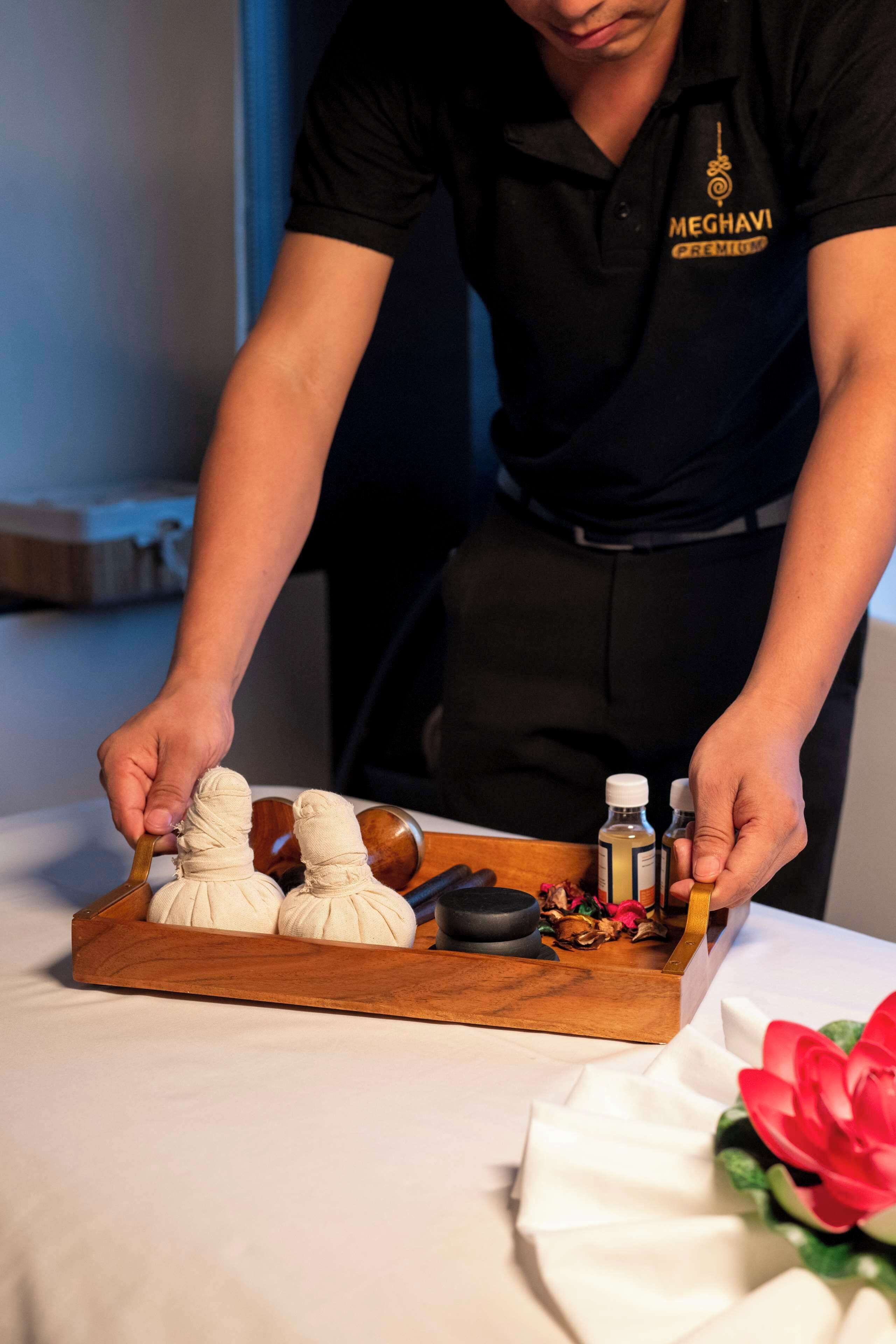 A person in a black shirt with a logo, handling a tray with massage tools and bottles.
