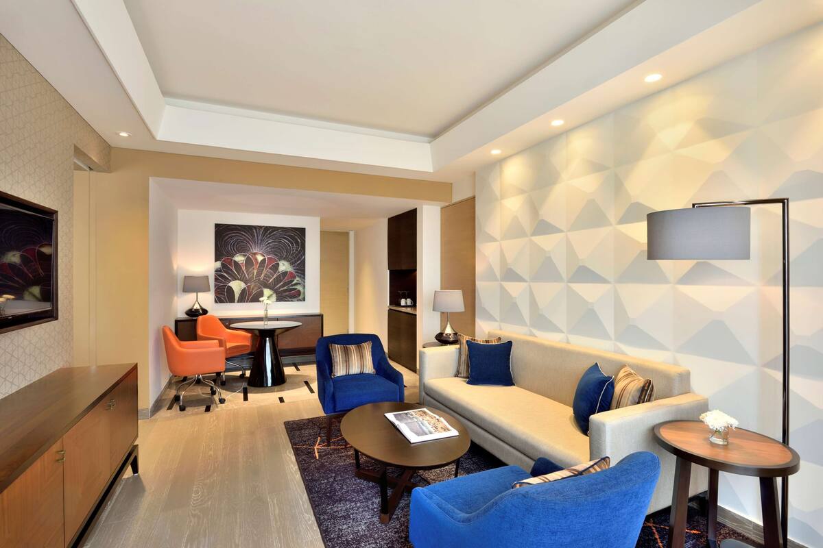 Una habitación de hotel moderna con sofá, dos sillones, una mesita de centro, televisor y un cuadro en la pared.