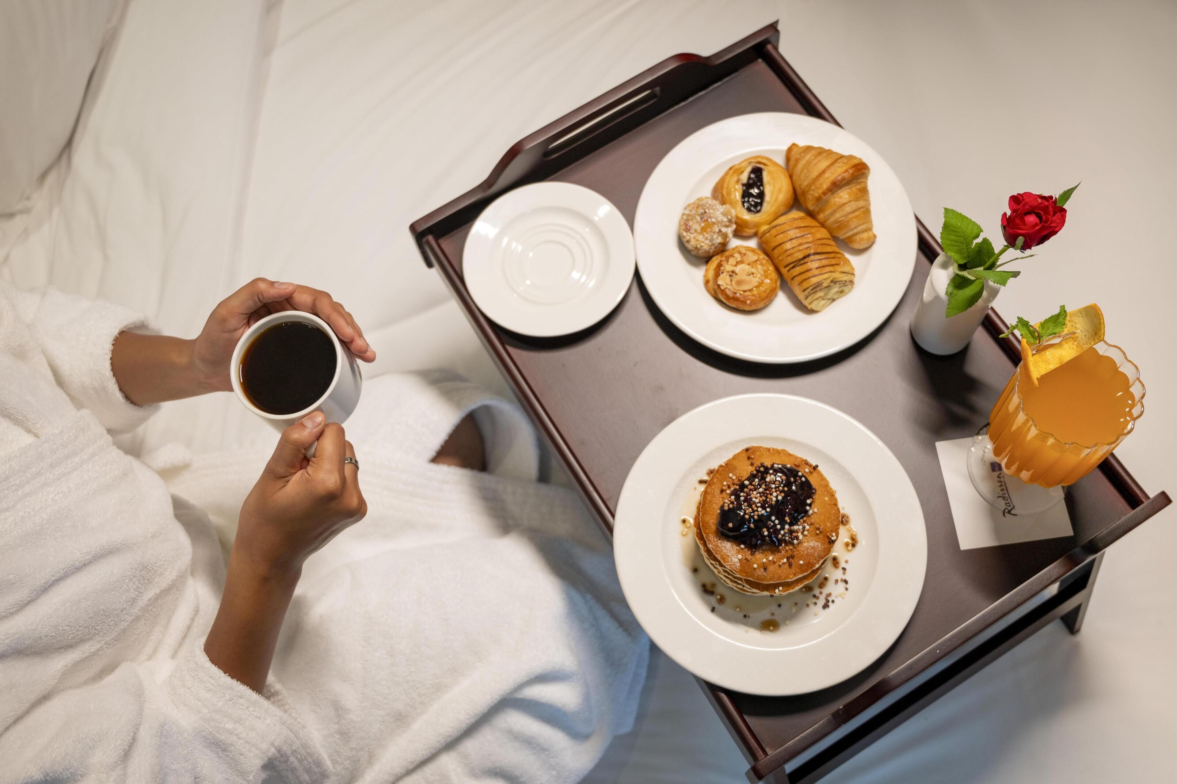 A tray with pastries, a coffee cup, and a rose on a bed.