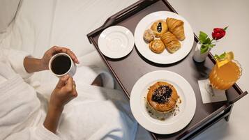 A tray with pastries, a coffee cup, and a rose on a bed.