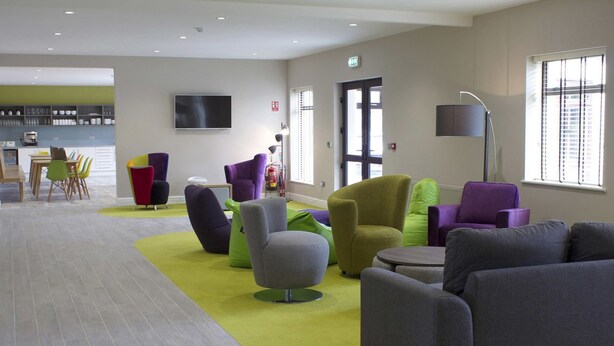 A modern lounge area with comfortable seating, a flat-screen TV, and a kitchen in the background. - The International (Knock)