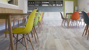 A modern dining area with a long wooden table and colorful chairs, a kitchen with white cabinets, and a green accent wall. - The International (Knock)