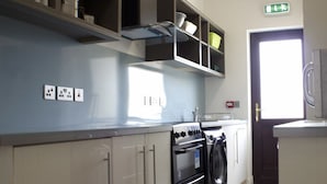 A kitchen with a stove, oven, and dishwasher. There is a window providing natural light and a door with an emergency exit sign. - The International (Knock)