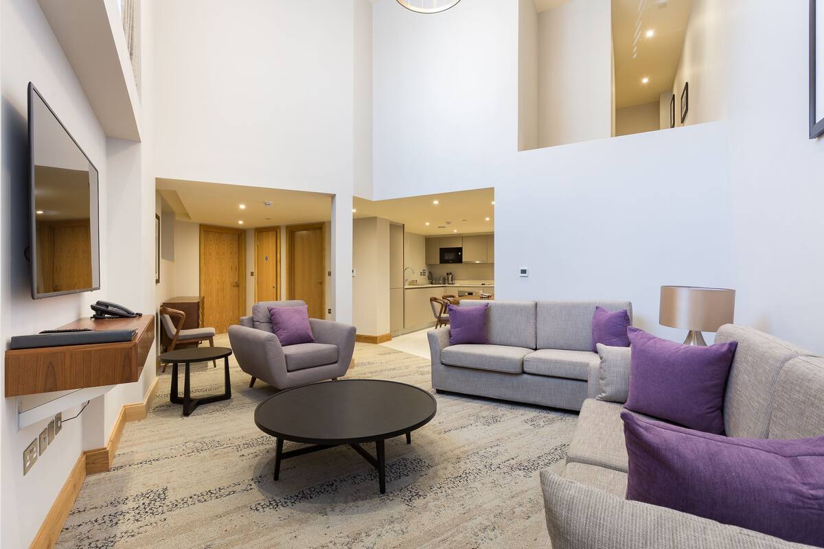 A spacious living area with a sofa, chairs, a coffee table, and a flat-screen TV mounted on the wall.