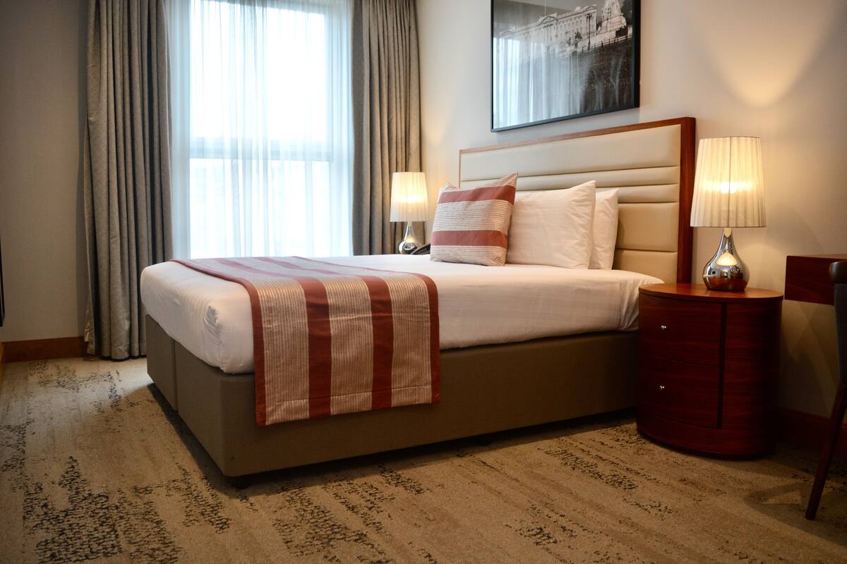 A hotel room with a large bed, two bedside lamps, a wooden nightstand, and a framed picture on the wall.