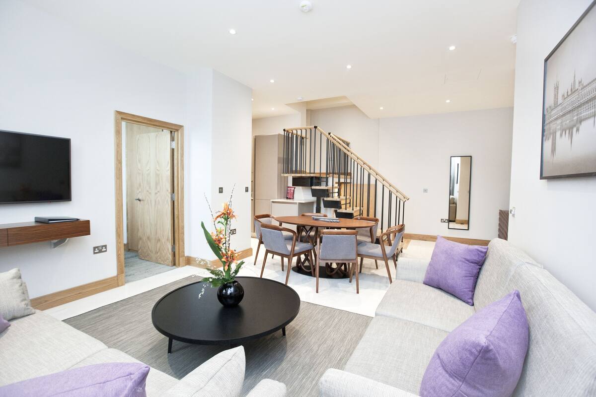 A modern living room with a sofa, coffee table, and a dining area with chairs and a table.