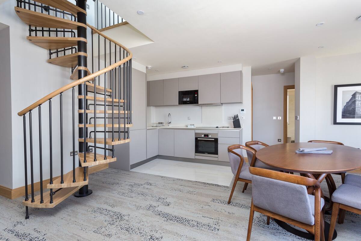 A modern kitchen with grey cabinets, a black microwave, and a wooden dining table with chairs.