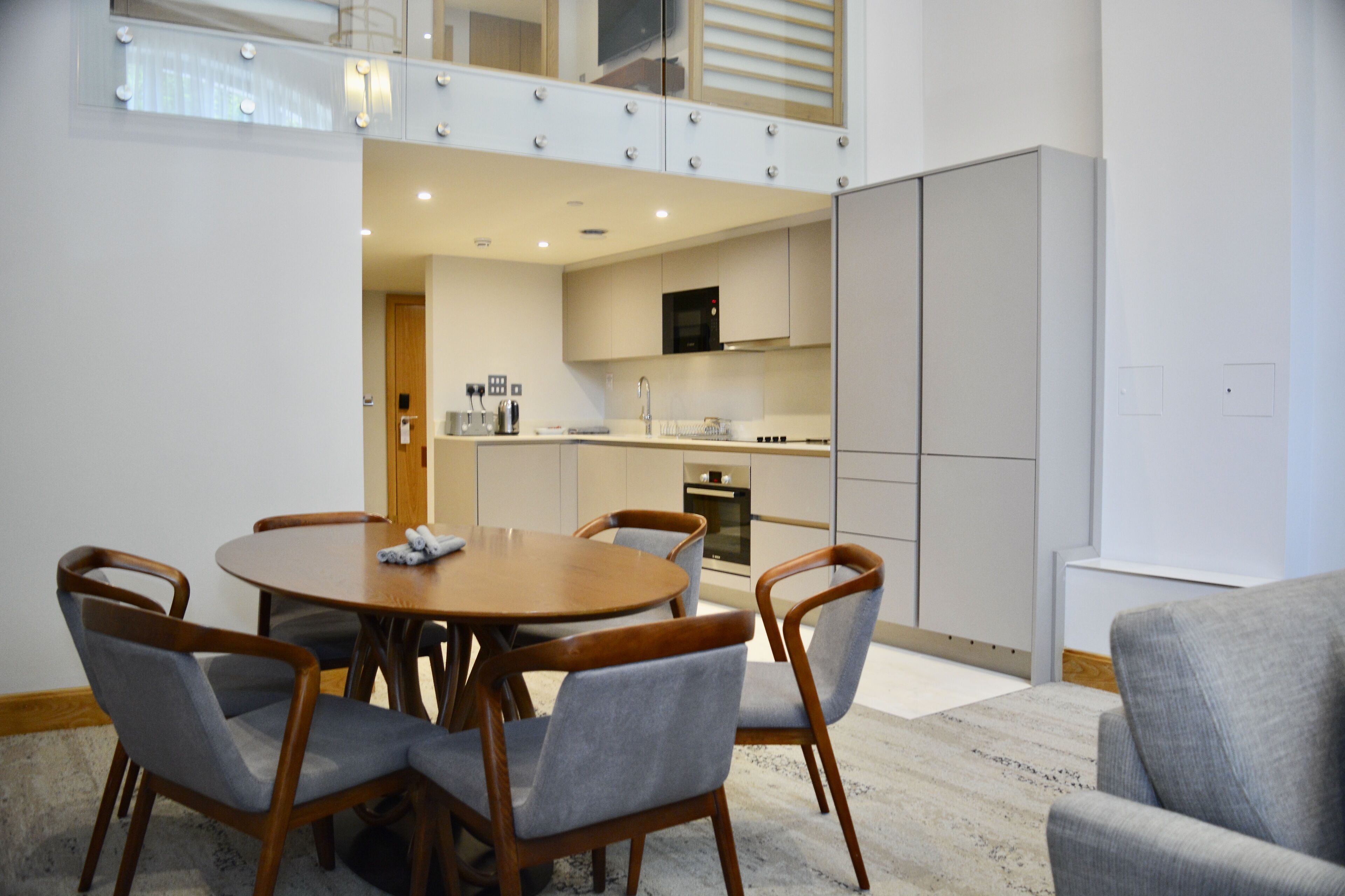 A modern kitchen with a dining area, featuring a round table and chairs, a built-in oven, and a television above the counter.