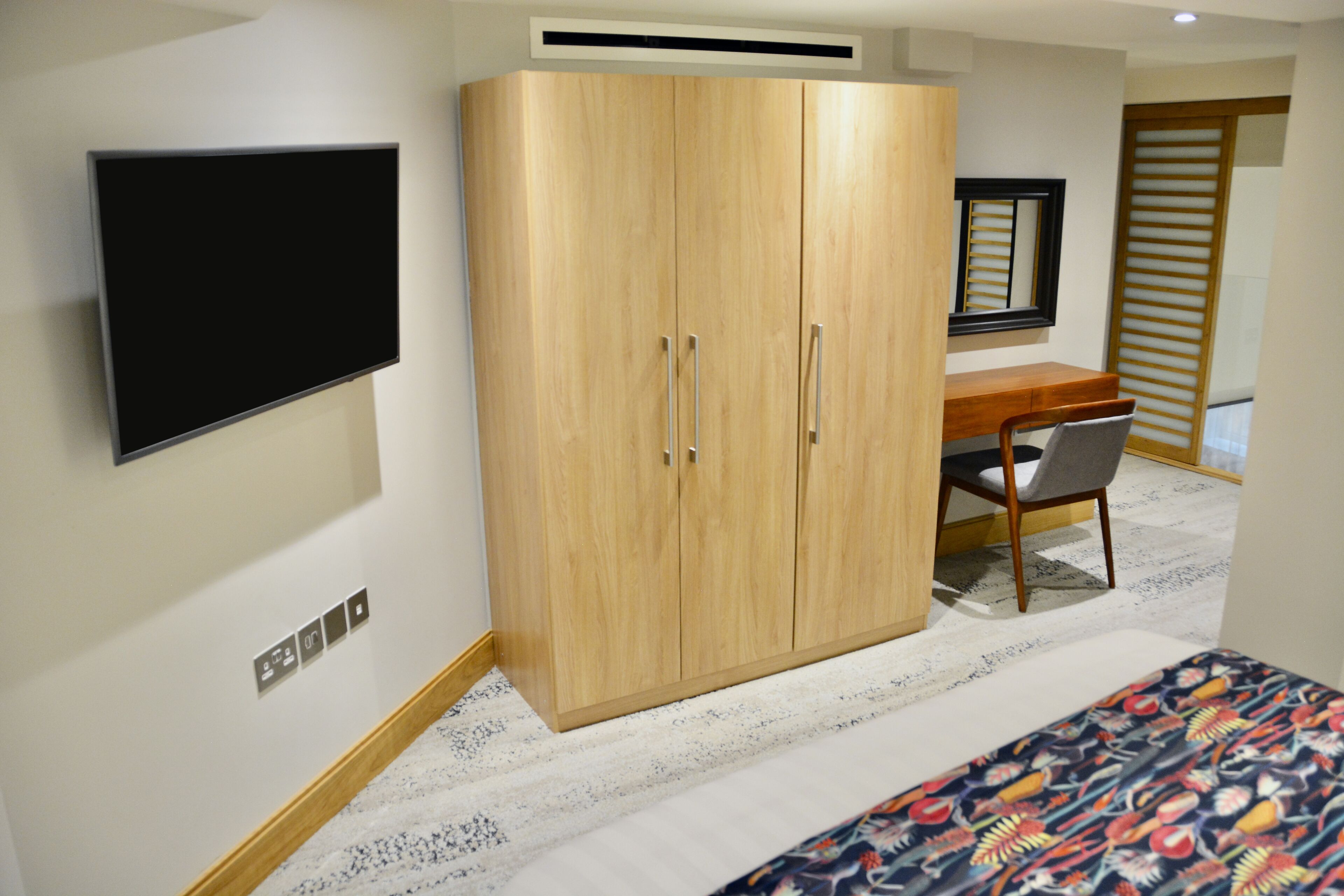 A room with a wardrobe, a desk, a chair, and a bed.