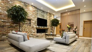 A modern living room with a brick fireplace, two grey sofas, a round coffee table, and a large potted plant.