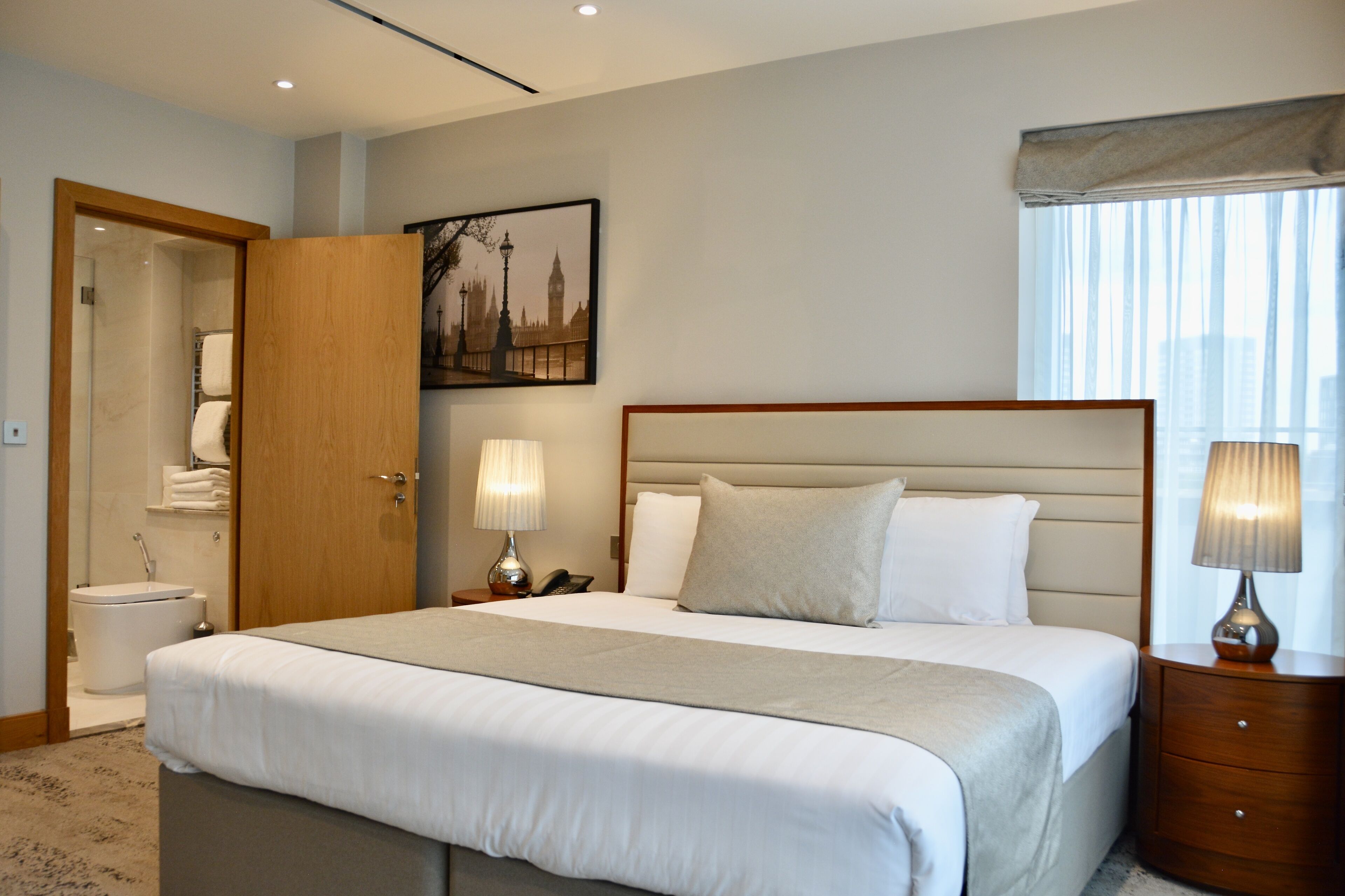 Une chambre d’hôtel avec un grand lit, des lampes de chevet, un tableau représentant un paysage urbain et une fenêtre avec des rideaux.
