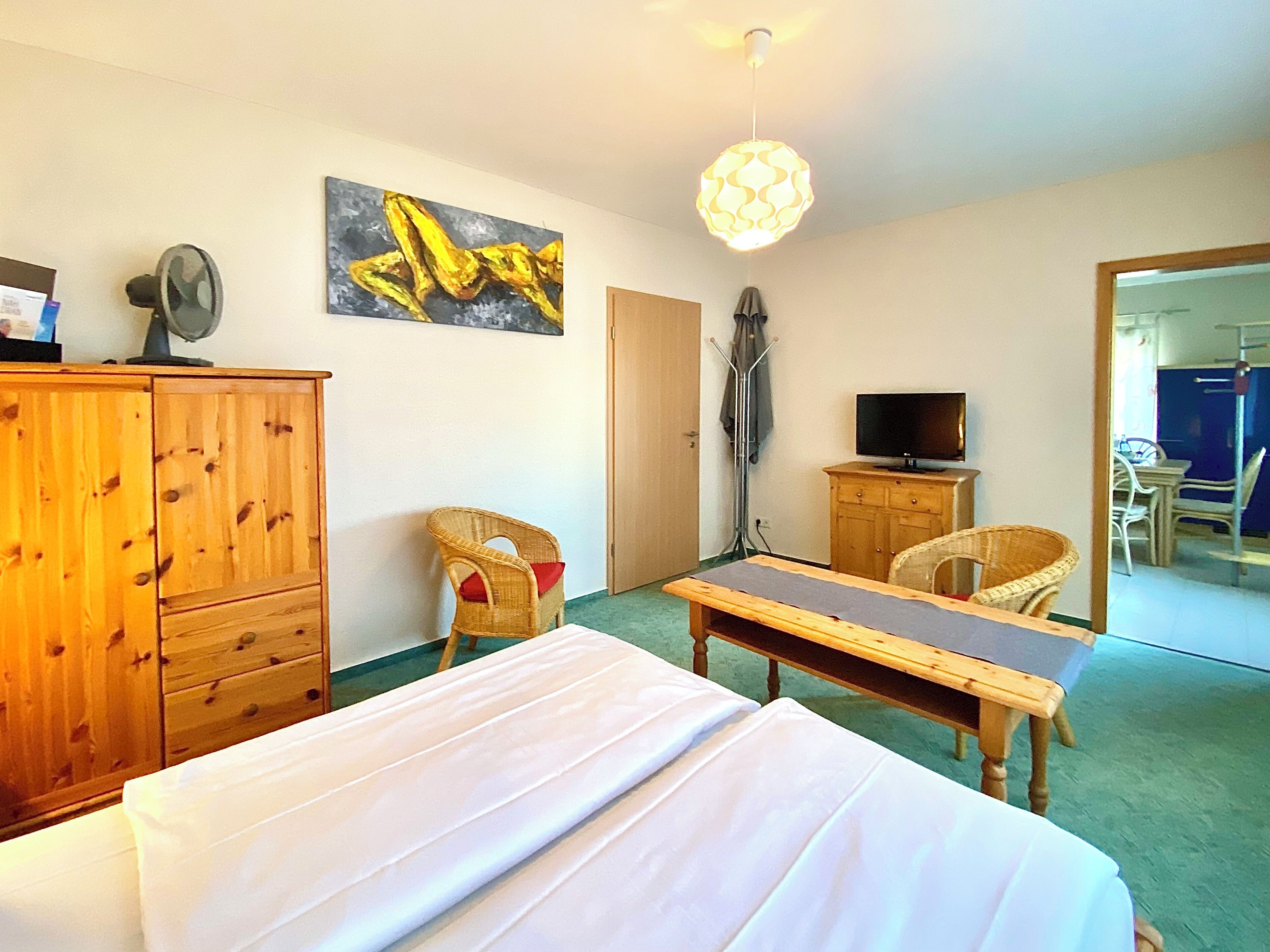 A hotel room with a bed, a desk, a television, a painting, and a wardrobe.