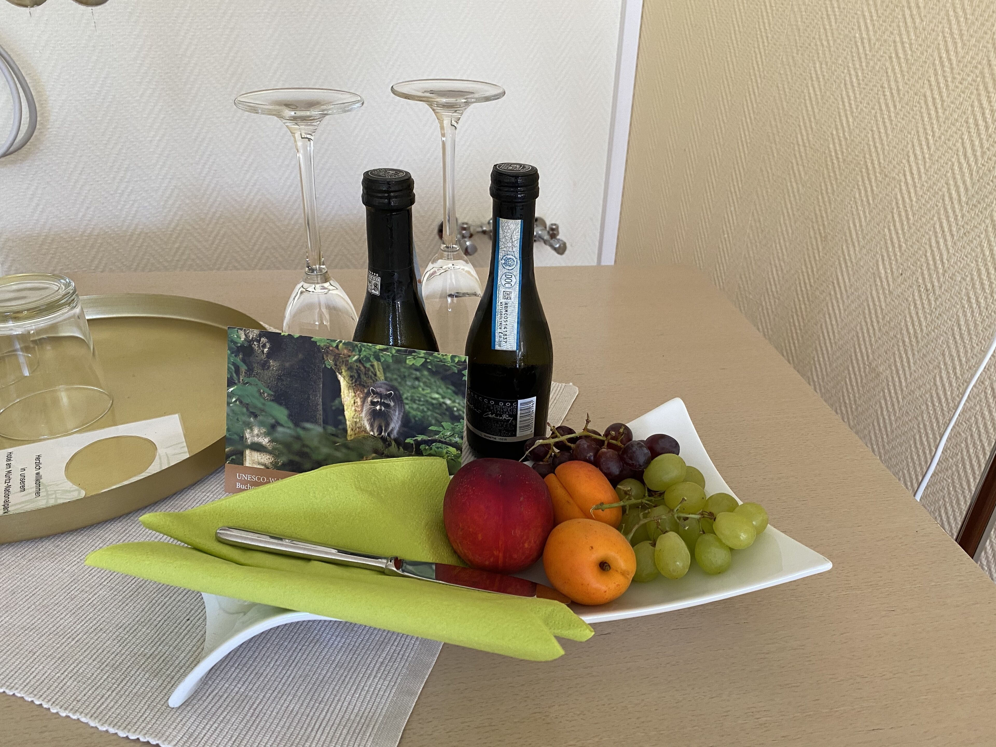 A table with a bottle of wine, two wine glasses, a plate with fruits, and a napkin.