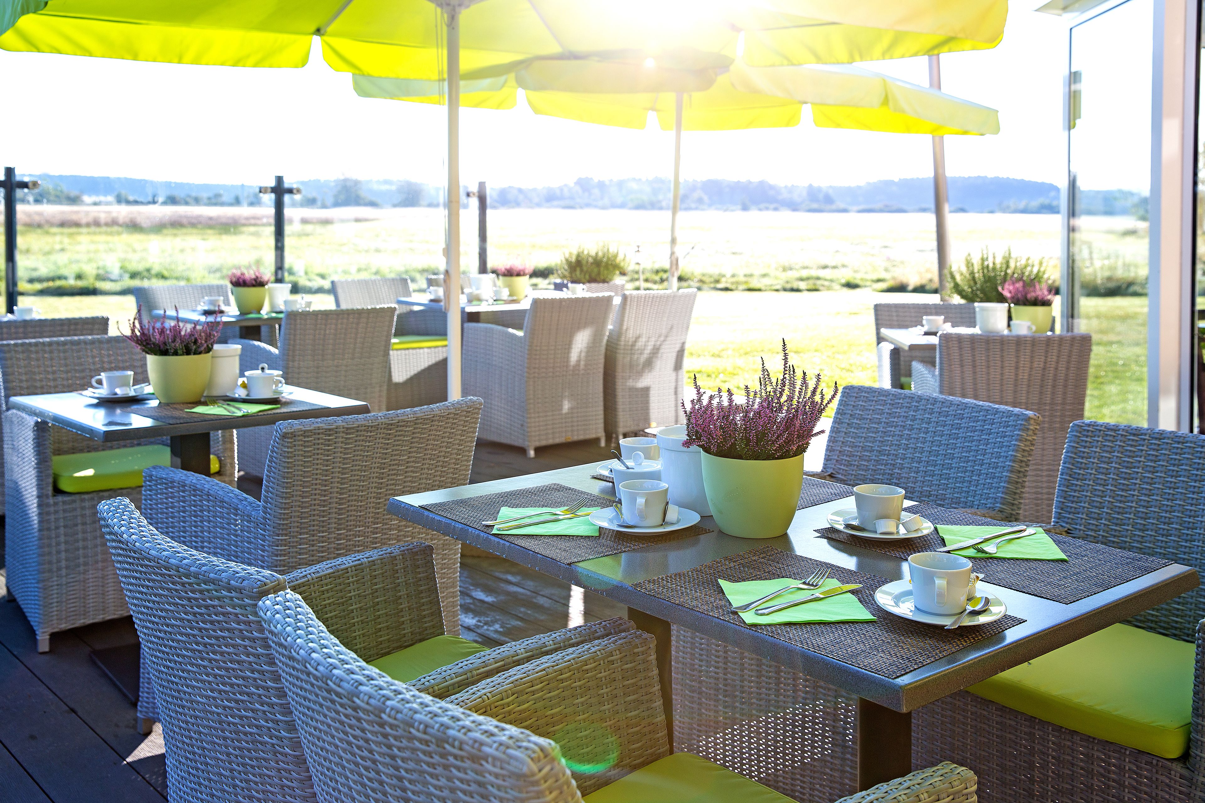 An outdoor patio with wicker furniture, yellow umbrellas, and a view of a field.