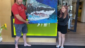 A man and a woman holding a large shark painting in a modern interior space with wooden floors and bright green accents. - Hotel am Müritz-Nationalpark (Waren (Müritz))