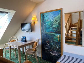 Een hotelkamer met een eethoek, een schilderij van eenden, een televisie en een trap.