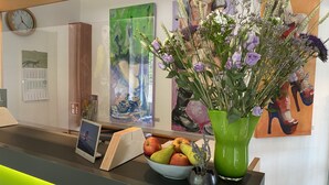 A reception desk with a clock, calendar, and artwork on the wall. - Hotel am Müritz-Nationalpark (Waren (Müritz))