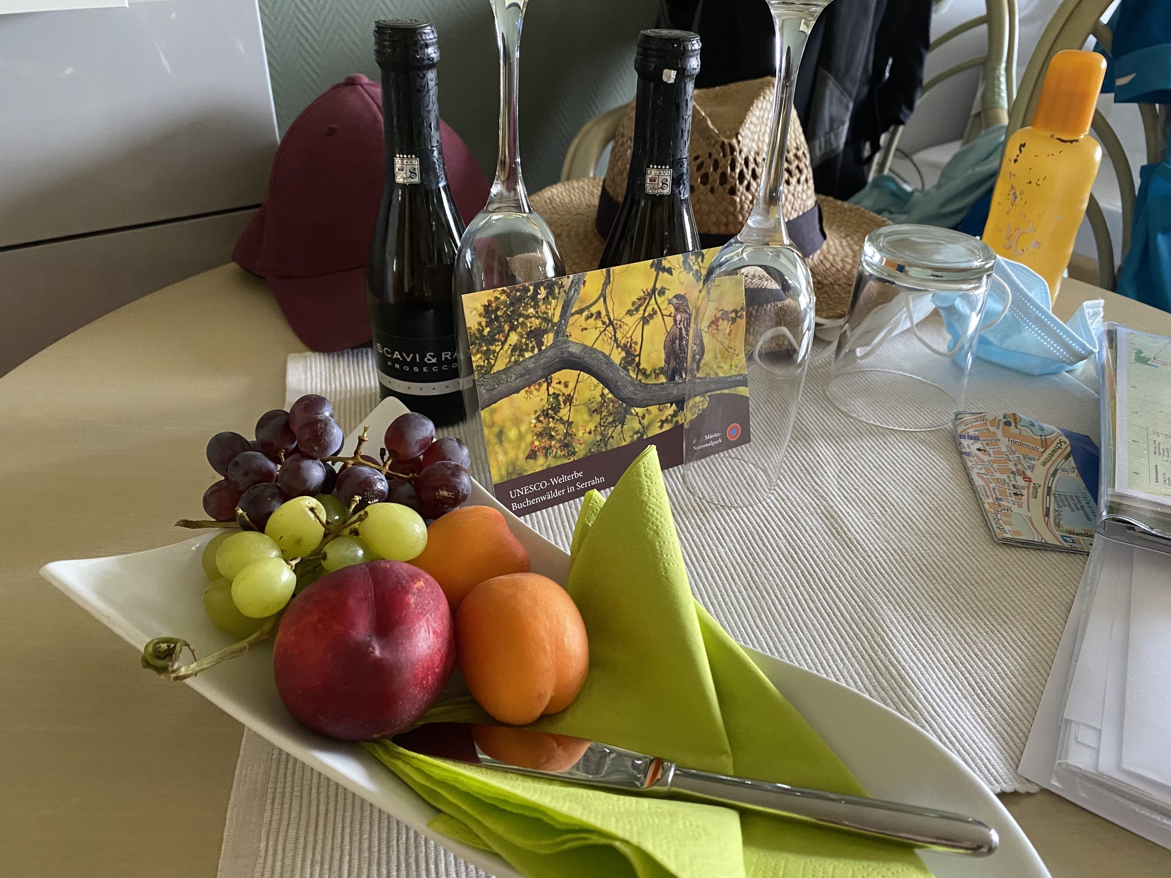 Ein Tisch mit einer Fruchtplatte, einer Weinflasche, einem Weinglas, einem Servietten und einem Messer.