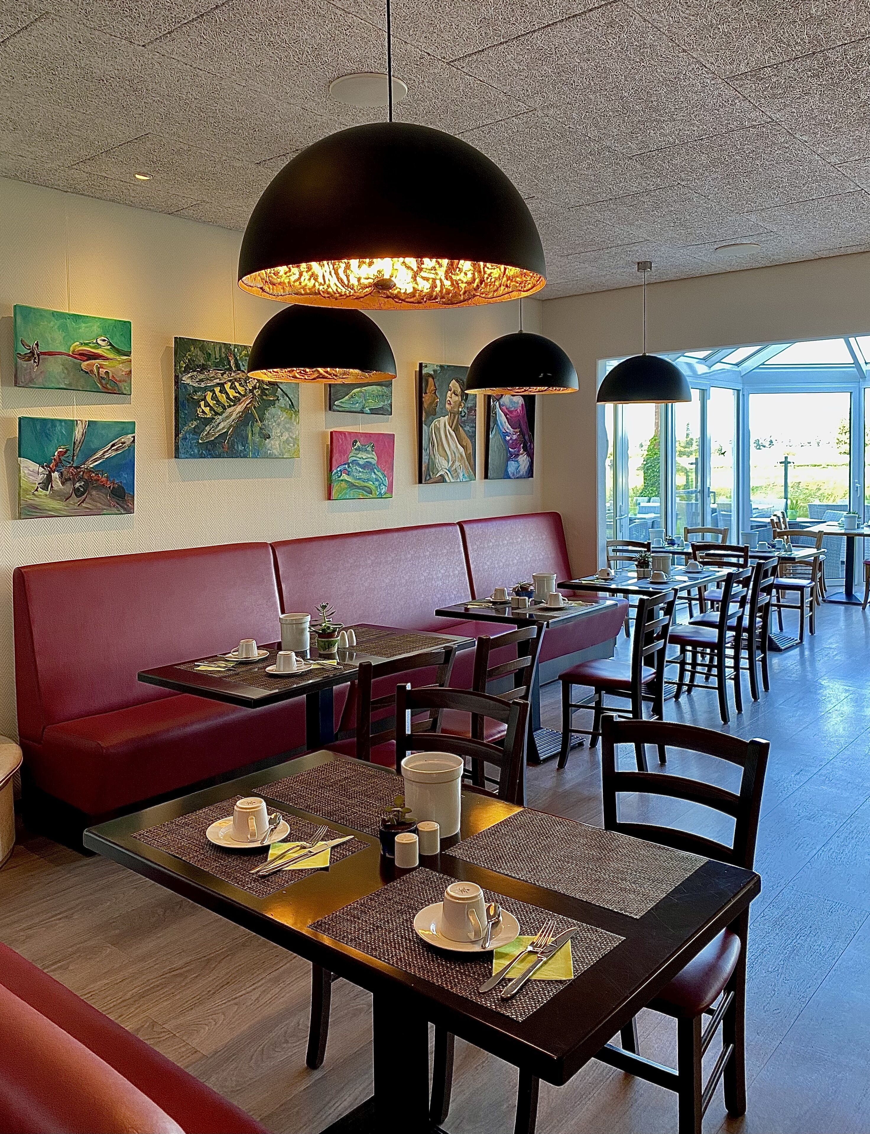Un restaurant avec des sièges rouges, des suspensions noires et des œuvres d’art accrochées aux murs.