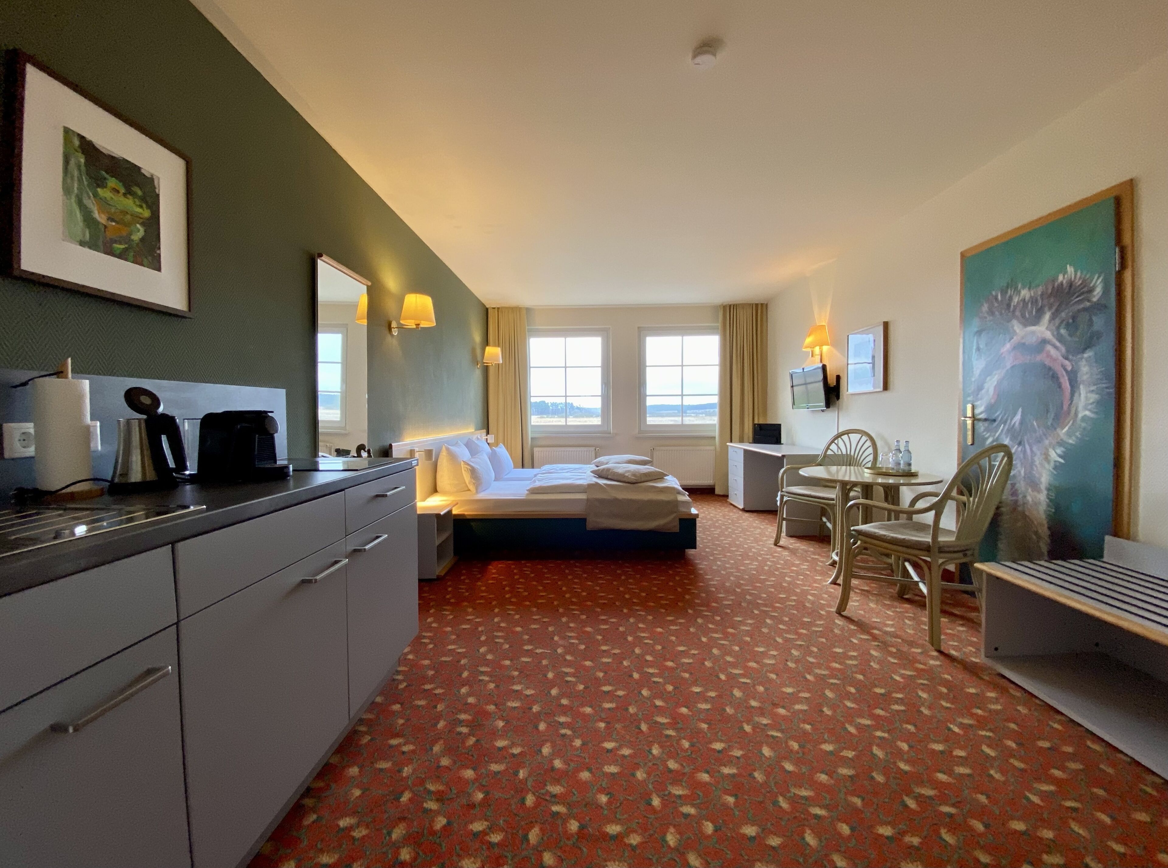 Ein Hotelzimmer mit Bett, Schreibtisch, Stuhl und einer Küchenzeile.