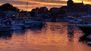 A marina with boats docked at sunset, buildings in the background, and calm water reflecting the sky. - Hotel am Müritz-Nationalpark (Waren (Müritz))