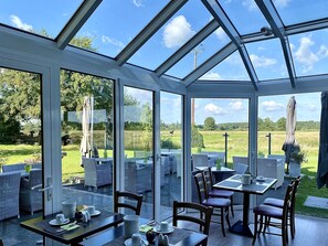 Une véranda aux murs de verre, avec un espace extérieur aménagé et une vue sur un champ verdoyant.