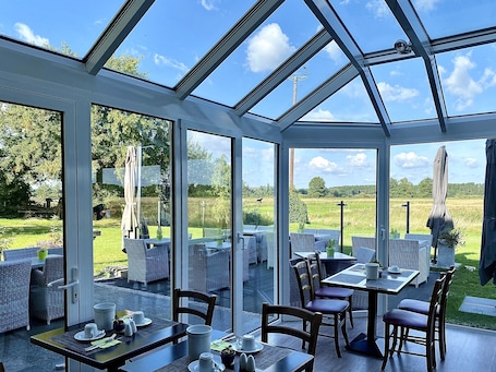 A conservatory with glass walls, outdoor seating, and a view of a grassy field.