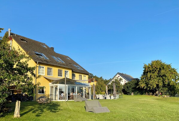 Een geel huis met een glazen conservatorium, een gazon en een houten terras.