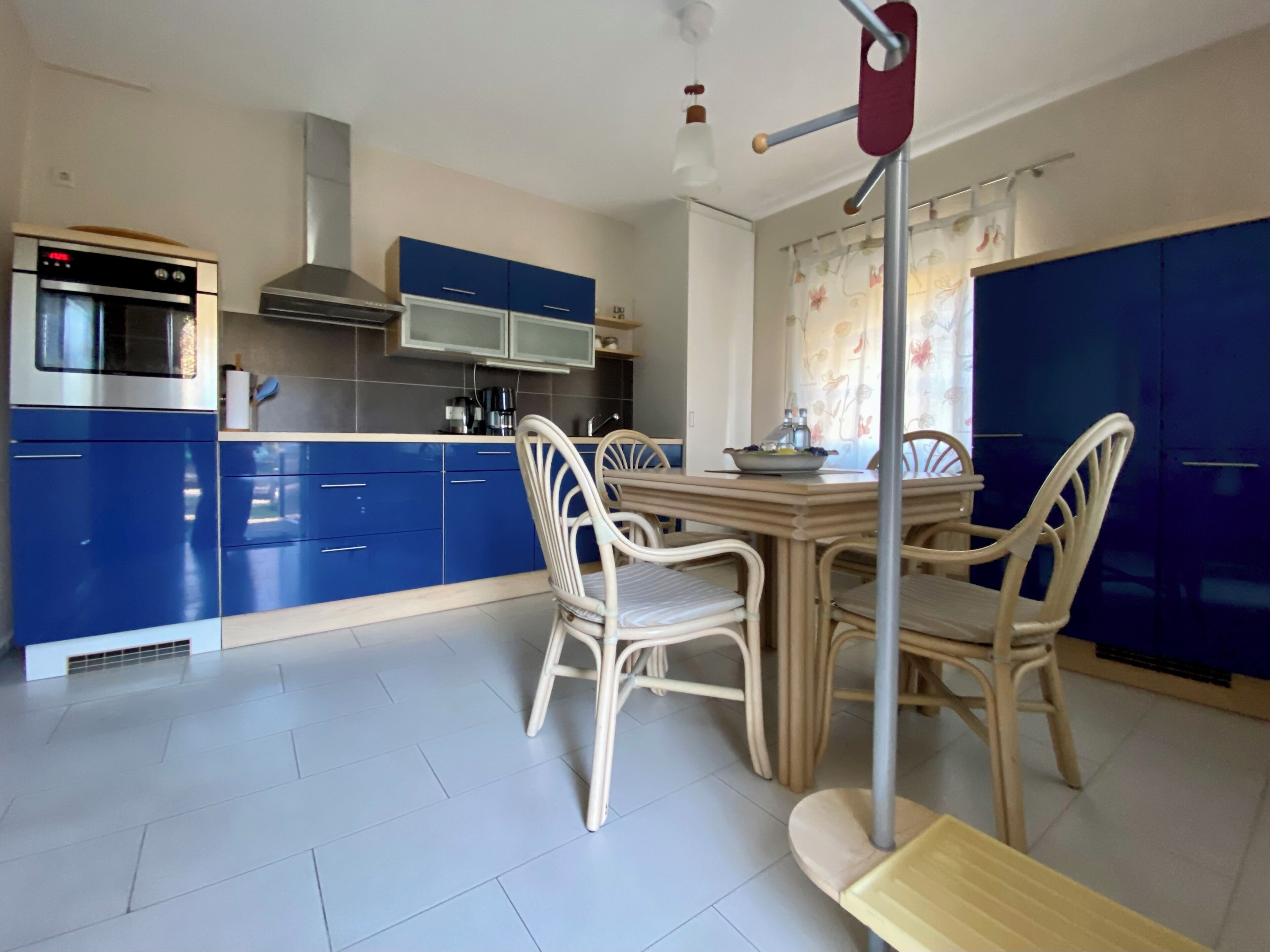 Une cuisine moderne avec des meubles de rangement bleus, une table à manger avec des chaises et un four encastré.